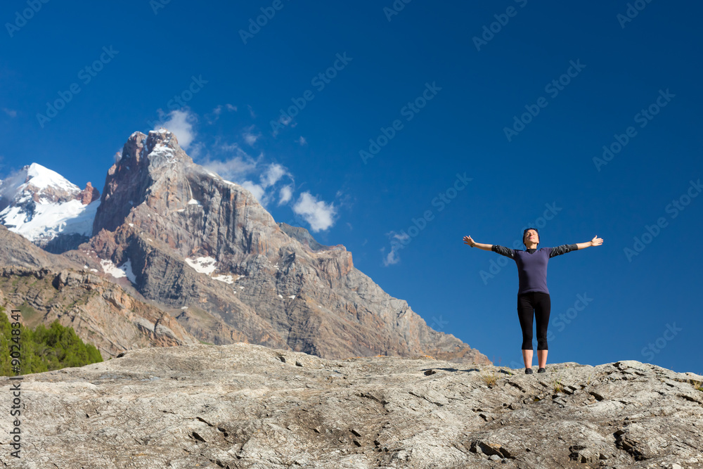 Young woman doing exercise Cute Girl Doing Yoga Fitness to Stretch Body Staying on High Rock at Mountain Panoramic Landscape Outdoor Sunny Sky Peaks Wilderness Country Smiling Beautiful Face Sunshine