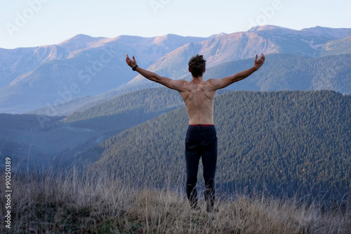 Back view of a man at the top of the mountain with raised hands and muscles on the back