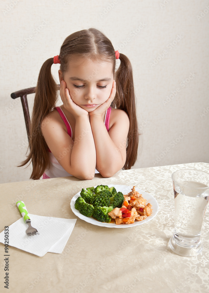 The girl looks indifferently at the dish with meat and broccoli