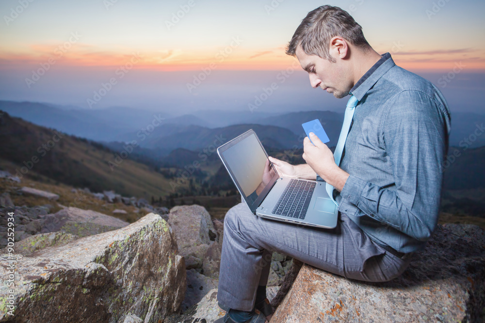 successful businessman on top of mountain, using a laptop