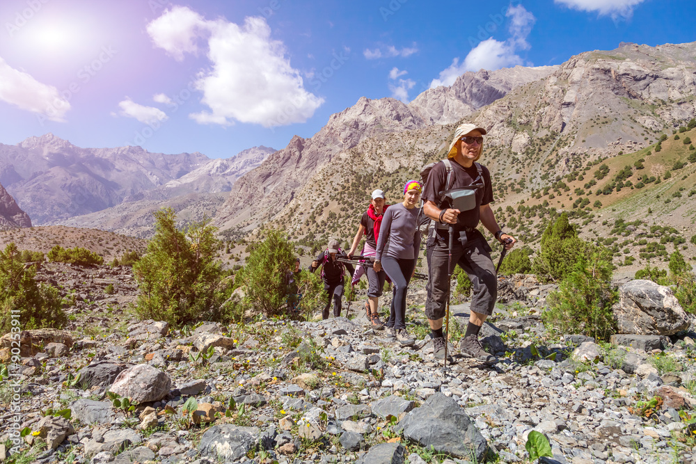 Group of people walking on trail Men and Women going up with Hiking Gear sporty Clothing on bright Mountain Landscape background with blue sky and Valley View Behind