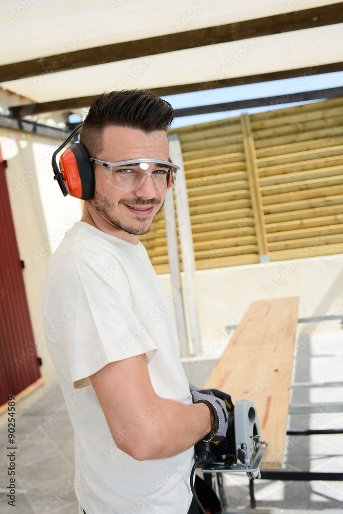 handsome young man carpenter working with electric tool on wood timber in construction site