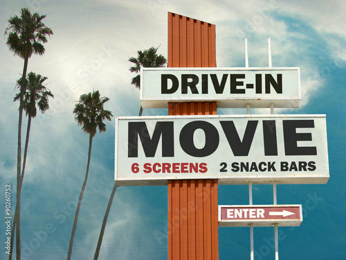 aged and worn vintage photo of drive in movie sign with palm trees