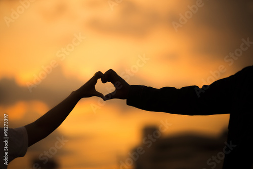 Happy couple making heart shape and sunset. Love unique concept.