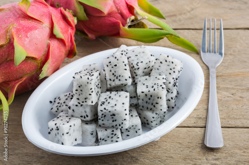 Dragon fruit slices in white cup on wooden background.