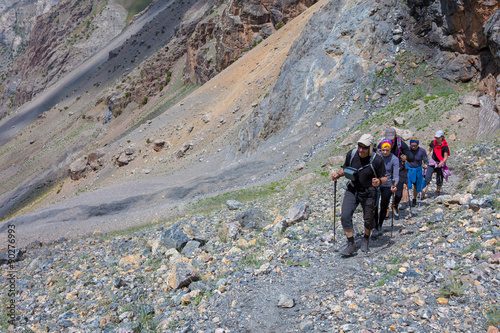 Group of Climbers Hard Walk Hiker Team Scramble Up on Rocky Trail with Severe Colored Steep on Background