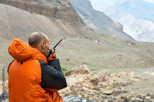 Man Talking on Radio Mountain Rescue Officer Holding Radio Walkie Talkie and Severe Mountain Landscape Background photo