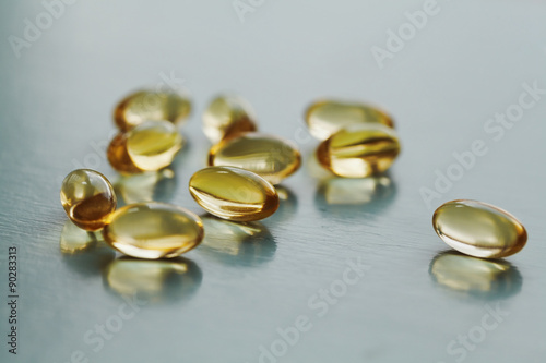 Yellow capsule with vitamin E tocopherol on blue surface, selective focus
