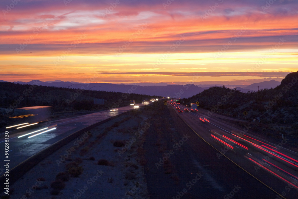 Cars drive Interstate 15 at sunset at California Nevada border looking west.