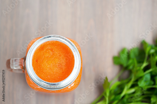 Healthy carrot smoothie in a mason jar with green parsley on wooden background. Shallow dof photo