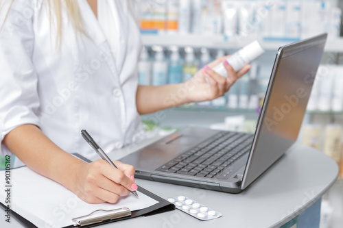 Close up of a druggist making notes from the laptop