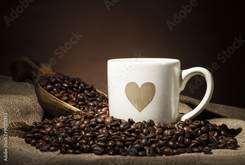 White cup with heart and coffee beans on dark background