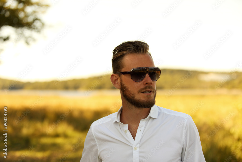 A man wearing a white shirt and dark sunglasses, standing against a large yellow field looking away from camera. A great sunny summer day. A man wearing a white shirt and dark sunglasses, standing against a large yellow field looking away from camera. A great sunny summer day.
