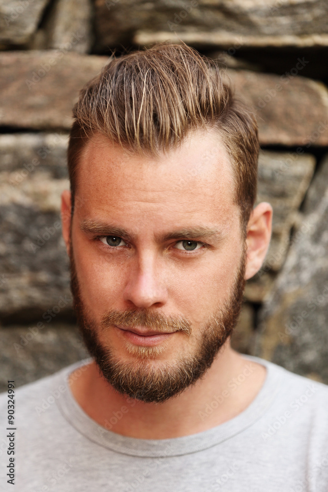 Fototapeta premium Attractive man wearing a grey sweater standing in front of a wall outside on a sunny summer day. 