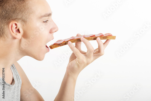 Young man eats big snack  opened mouth  side view