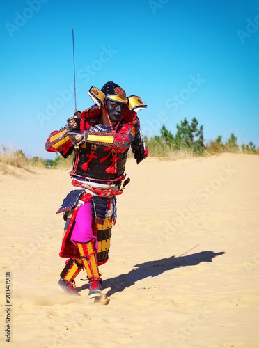 Man in samurai costume with sword running on the sand. 