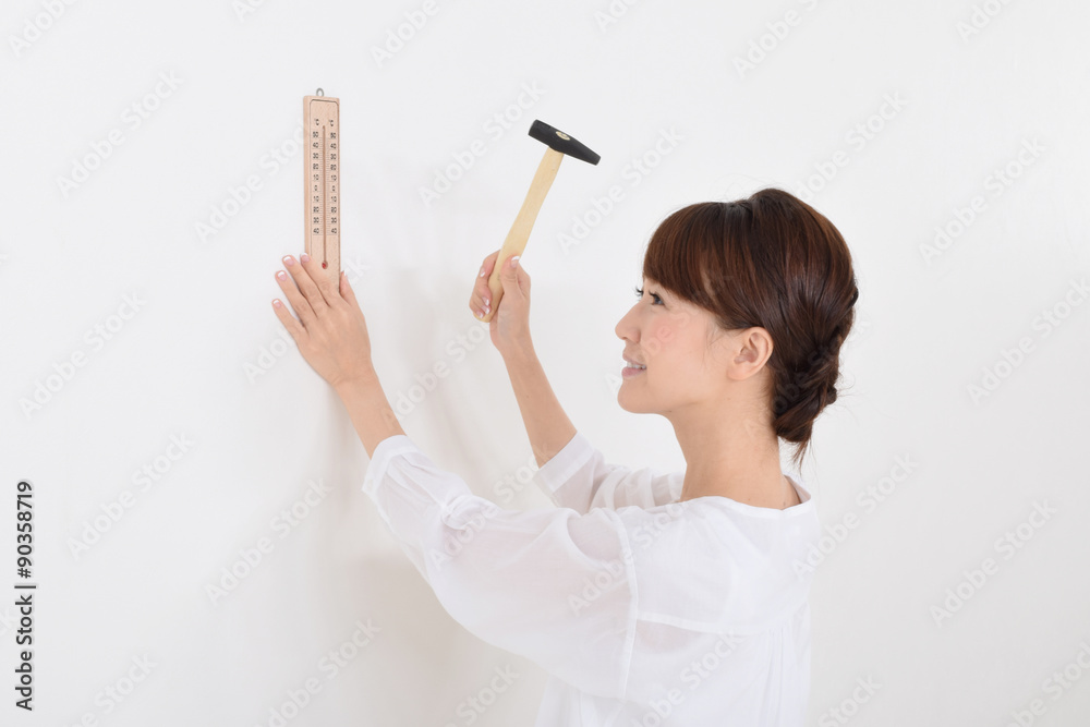 金づちで壁に温度計を取り付ける女性 金づちで壁に温度計を取り付ける女性