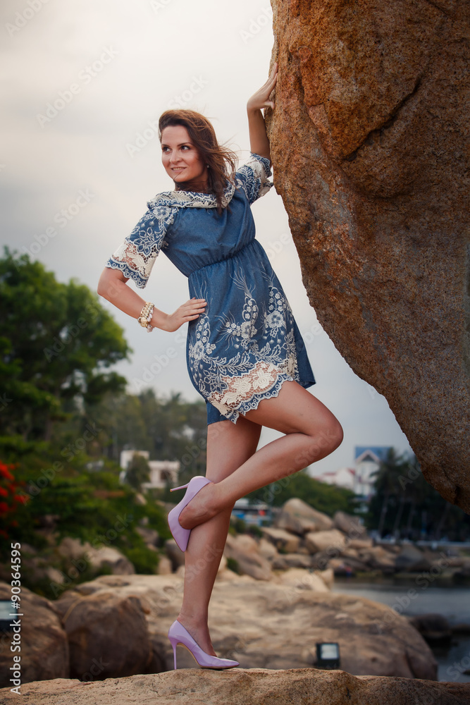 brunette girl in short frock high-heel shoes stands under rock