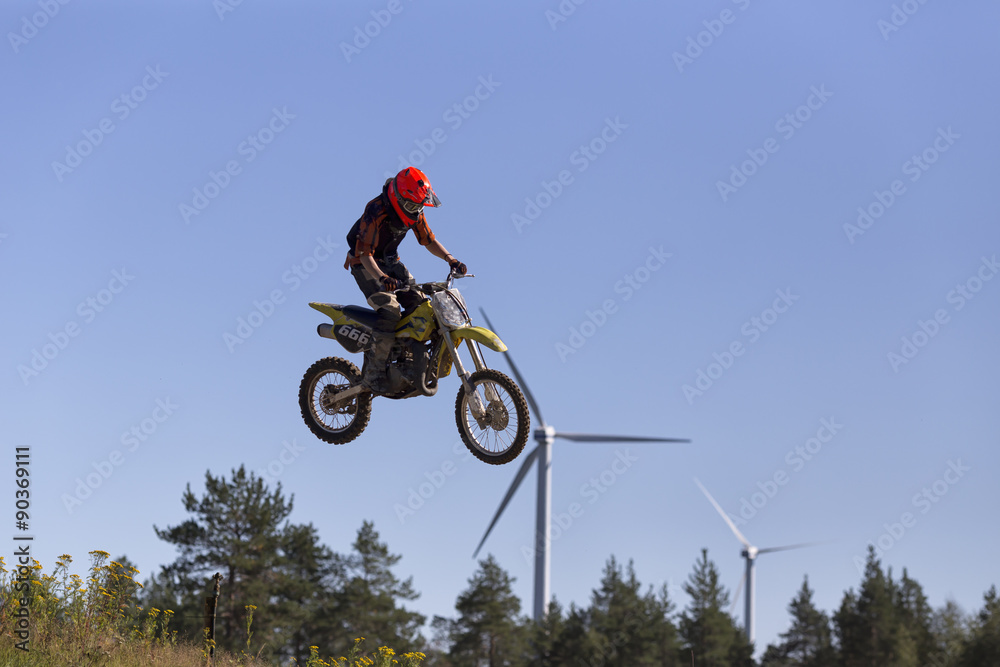Obraz premium A motorcycle jumper in the air an two wind turbines in the background