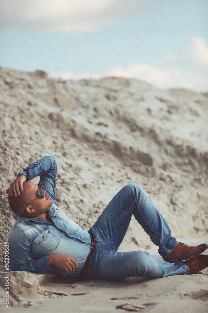 young guy in jeans clothes lying on the sand in Turkey