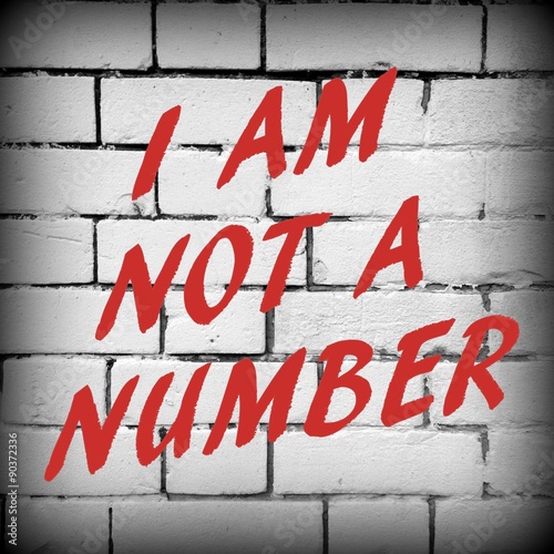 The phrase I Am Not a Number in red text on a brick wall background. Processed in black and white with a vignette added for effect