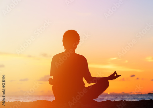 Silhouette of young man meditating at sunset