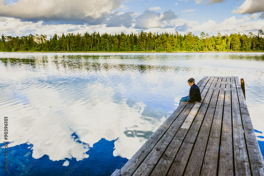 Boy sitting on a wooden pier and watching the water