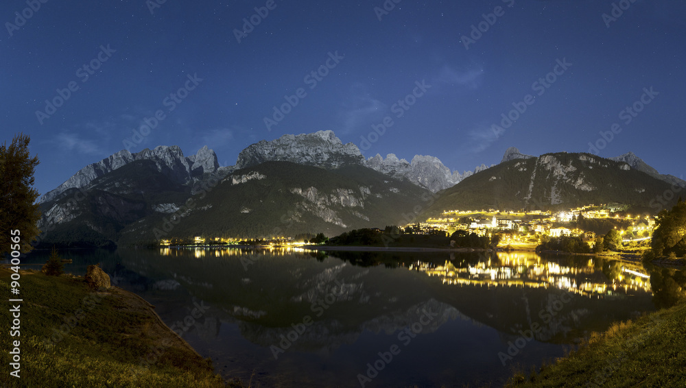 Night landscape on the Moveno lake and city with Dolomiti of Brenta Group in background at the moonlight