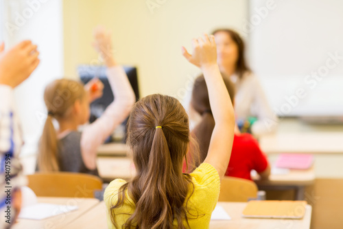 group of school kids raising hands in classroom