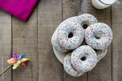 Donuts with white glaze and colorful sprinkles on rustic table