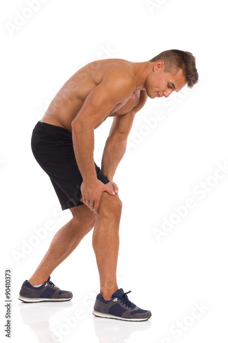 Knee injury. Young muscular man holding knee in pain. Full length studio shot isolated on white.