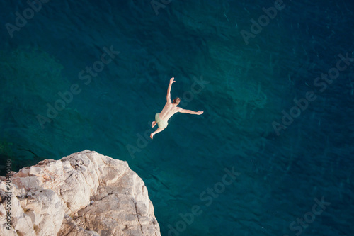 Young man jumping from cliff into sea.