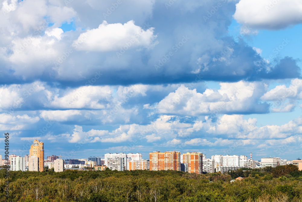 low blue clouds over green forest and city