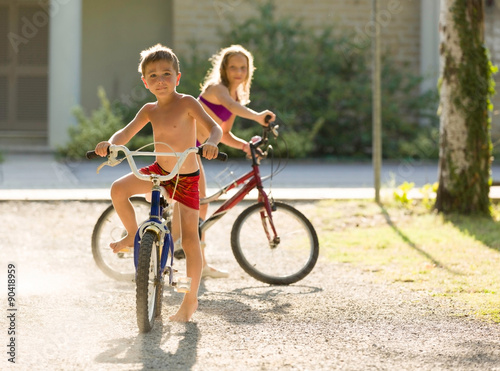 Blonde children ride bycicle under sunlight