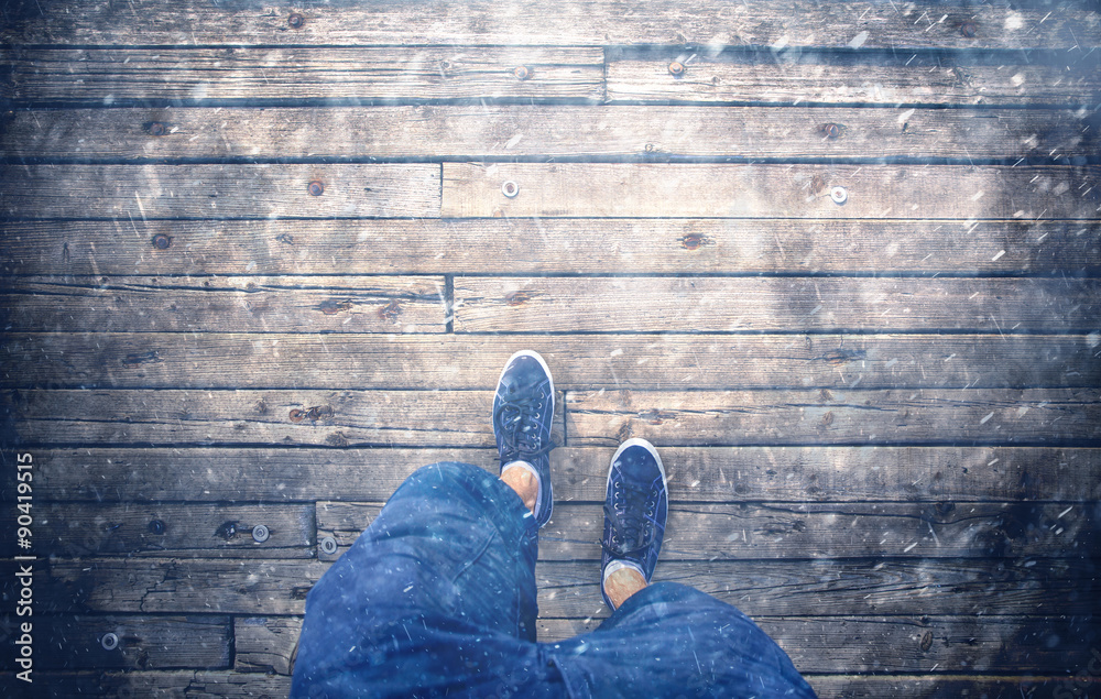 A man walking on rainy and snowy day on aged wooden floor, point of view perspective. Heavy rain and a man with blue shoes and shorts jeans walking on wooden bridge. Conceptual photo. A man walking on rainy and snowy day on aged wooden floor, point of view perspective. Heavy rain and a man with blue shoes and shorts jeans walking on wooden bridge. Conceptual photo.