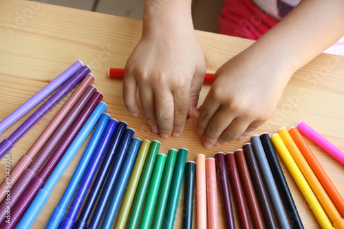 Close up of colored pens arranged on the table with the child's hands