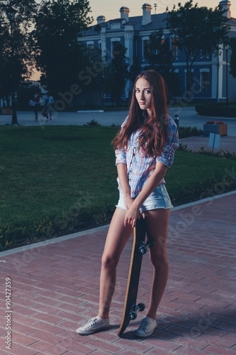 Young slim girl standing with her skateboard outdoors