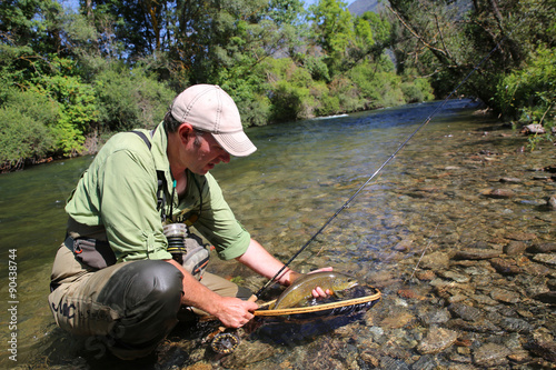Fly-fisherman in water catching brown trout fish