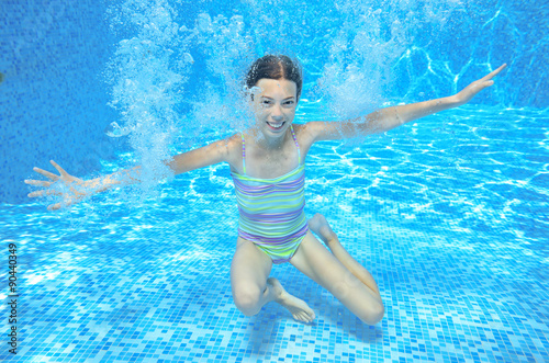 Child swims in pool underwater, happy active girl has fun in water