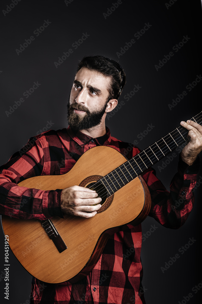 Portrait of a happy young man with beard playing guitar against