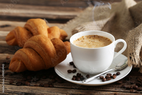 Delicious croissants with cup of coffee on brown wooden backgrou