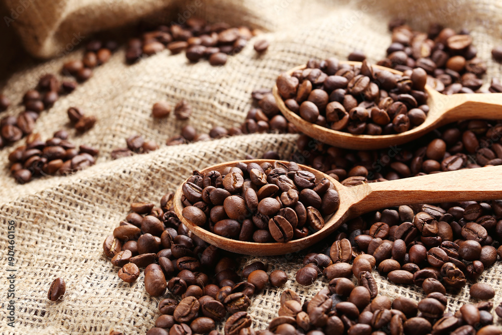 Coffee beans in wooden spoon on a sack, close up