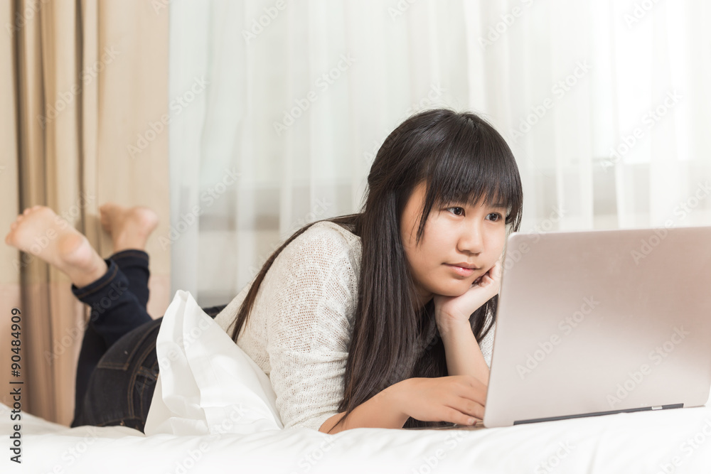 Asian Woman lying on a bed at home and she works on a laptop Asian Woman lying on a bed at home and she works on a laptop