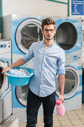 Fotografija young man holding a laundry basket in launderette