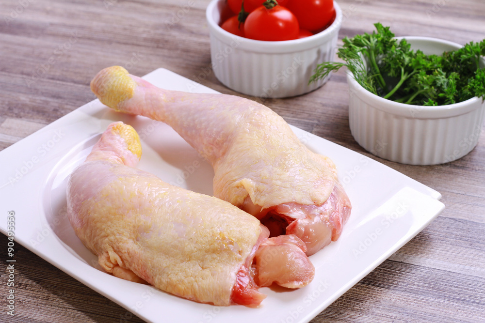 Raw chicken legs decorated with salad and cherry tomatoes on white plate. Diet food, healthy lifestyle Raw chicken legs decorated with salad and cherry tomatoes on white plate. Diet food, healthy lifestyle