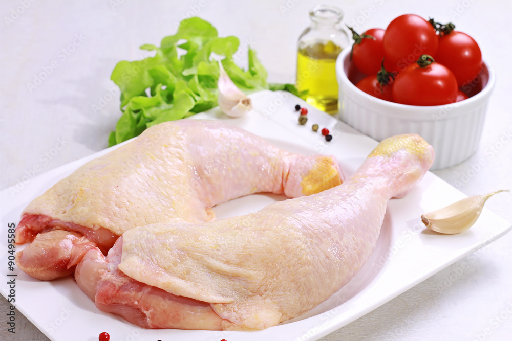 Raw chicken legs decorated with salad, olive oil and cherry tomatoes on white plate. Diet food, healthy lifestyle Raw chicken legs decorated with salad, olive oil and cherry tomatoes on white plate. Diet food, healthy lifestyle