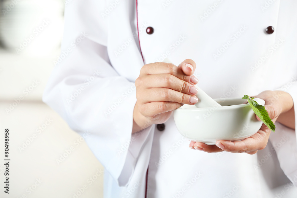 Cook hands with mortar with herbs on bright background Cook hands with mortar with herbs on bright background