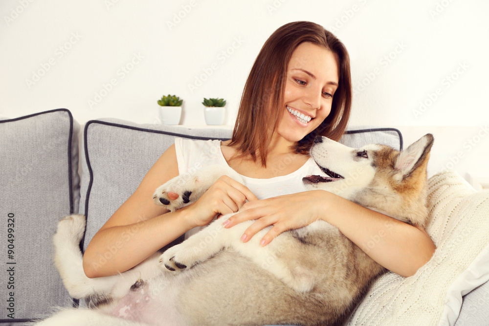 Woman sitting with her malamute dog on sofa in room Woman sitting with her malamute dog on sofa in room