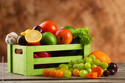 Heap of fresh fruits and vegetables in crate on wooden table close up
