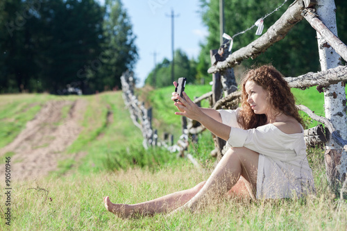 Pretty Caucasian woman making selfie while wearing a shirt over her naked body, sitting on countryside